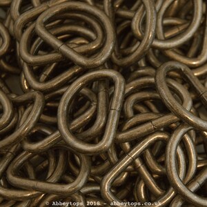 May include: A close-up of a pile of gold-toned metal D-rings. The rings are all the same size and are arranged in a random pattern.