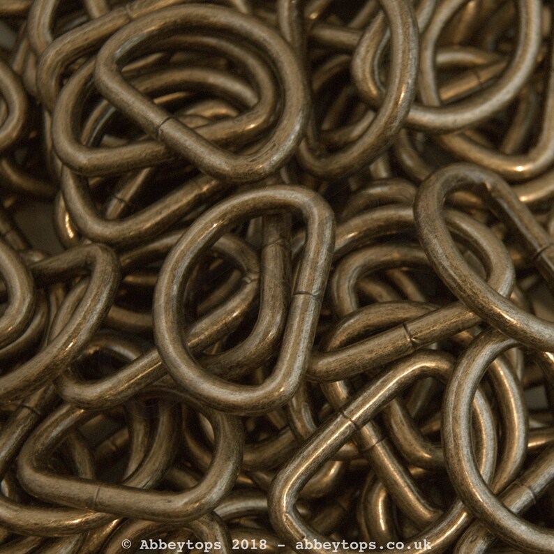 May include: A close-up of a pile of gold-toned metal D-rings. The rings are all the same size and are arranged in a random pattern.