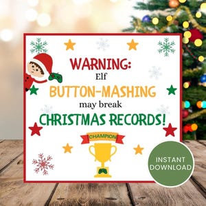 Op de afbeelding: Een kerstbord met een rode rand. Het bord bevat de tekst "WARNING: Elf BUTTON-MASHING may break CHRISTMAS RECORDS!" samen met een cartoon elf, sterren, sneeuwvlokken en een trofee. Een groene cirkel zegt "INSTANT DOWNLOAD".