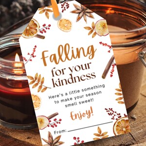 May include: A lit candle in a glass jar next to a gift tag with the words "Falling for your kindness." The tag has watercolor illustrations of fruit, leaves, and cinnamon sticks. The tag reads "Here's a little something to make your season smell sweet! Enjoy!"