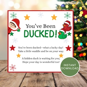 May include: A square Christmas-themed card with a red border, featuring the text You've Been DUCKED! in black and green. Illustrations include a cartoon elf, two rubber ducks wearing Santa hats, yellow stars, and green and red snowflakes.