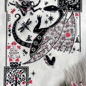 May include: A cross-stitch embroidery on white fabric featuring a large black dragon with patterned wings, a small winged figure, dragonflies, and a tree. The design uses black, white, and red thread to create intricate geometric and floral motifs.