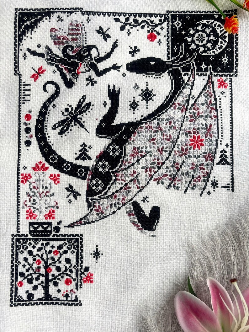 May include: A cross-stitch embroidery on white fabric featuring a large black dragon with patterned wings, a small winged figure, dragonflies, and a tree. The design uses black, white, and red thread to create intricate geometric and floral motifs.
