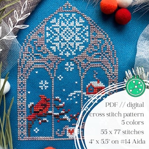 May include: A cross-stitch pattern on blue fabric depicts a winter scene with a red bird, snow-covered branches, and a small house. The pattern is 4" x 5.5" and uses 5 colors. The text reads "PDF // digital cross stitch pattern".