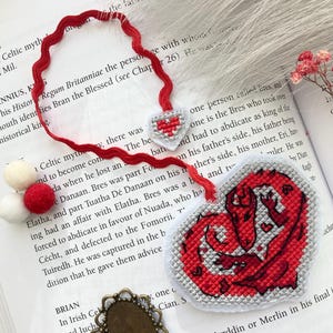 Peut inclure: Marque-page fait main en forme de c&oelig;ur rouge et blanc avec un motif de dragon. Le marque-page comporte un ruban rouge et des pompons. Le c&oelig;ur mesure environ 7.6 cm de large.