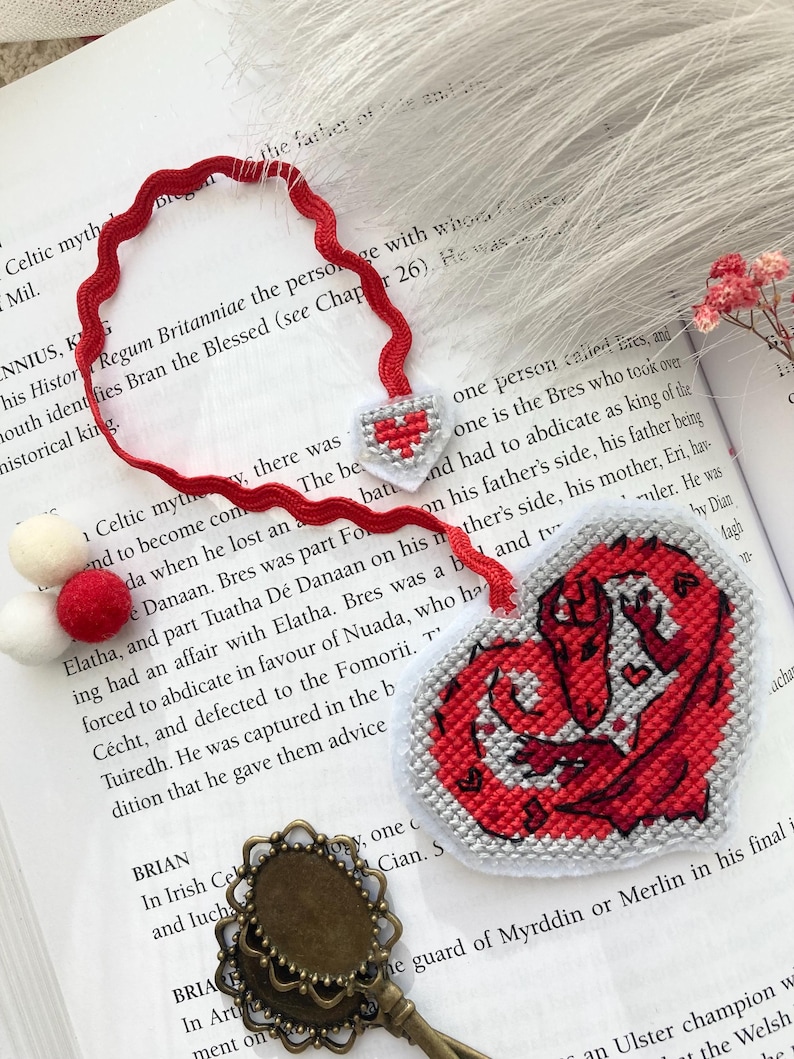Peut inclure: Marque-page fait main en forme de c&oelig;ur rouge et blanc avec un motif de dragon. Le marque-page comporte un ruban rouge et des pompons. Le c&oelig;ur mesure environ 7.6 cm de large.