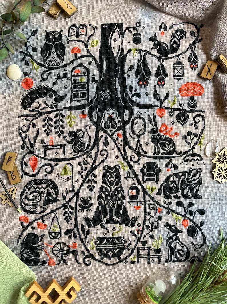 May include: A detailed cross-stitch design featuring a central tree with various woodland creatures and objects. The design includes an owl, squirrel, bats, bear, and other animals, with orange and green accents on a neutral background.