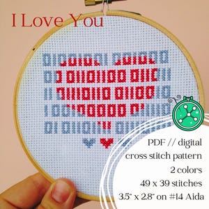 Könnte beinhalten: Ein Kreuzstich-Stickrahmen mit den Worten "I Love You" in rotem und blauem Binärcode. Das Muster ist 8,9 cm x 7,1 cm groß auf Aida-Stoff Nr. 14. Das Design enthält ein Herzsymbol und ist ein digitales Kreuzstichmuster.