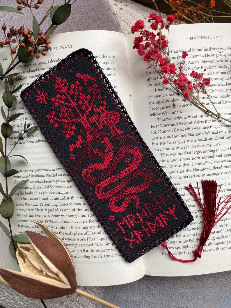 K&ouml;nnte beinhalten: Schwarz-roter bestickter Lesezeichen mit einem Baum- und Schlangenmuster. Das Lesezeichen hat einen schwarzen Rand und eine rote Quaste. Der Text "MRADI XHMXY" ist auf dem Lesezeichen zu sehen.