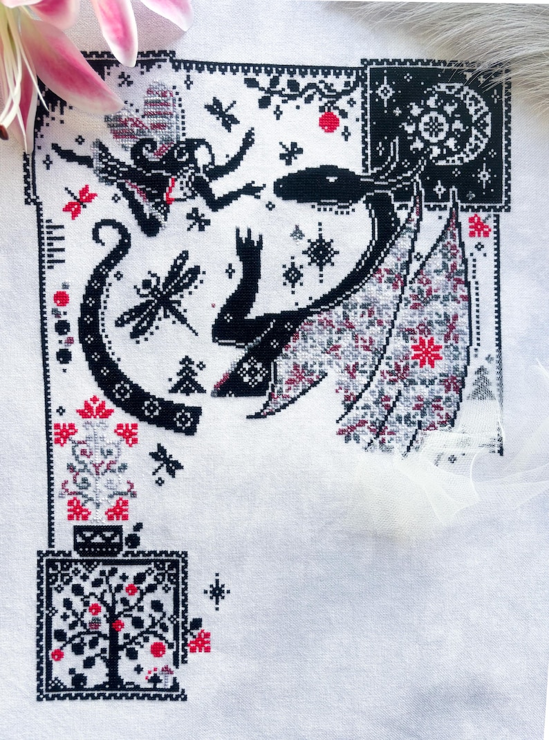 May include: A white fabric piece featuring a black, red, and gray cross-stitch pattern. The design includes a winged creature, a fairy, dragonflies, a tree, and a moon. The intricate embroidery displays geometric borders and floral motifs.