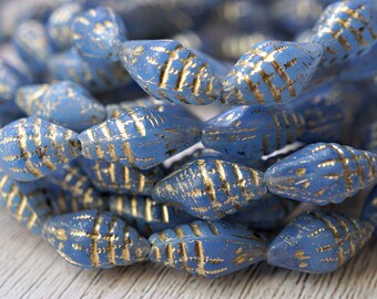May include: Close-up of a strand of blue glass beads with gold accents. The beads are oval-shaped with a textured surface and a gold grid pattern. The beads are strung together on a white string.