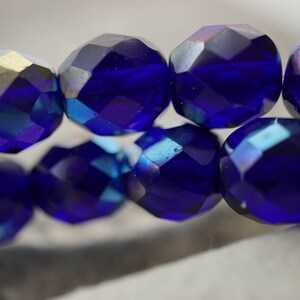 Puede incluir: Una hebra de cuentas de vidrio facetadas de color azul oscuro con brillo iridiscente. Las cuentas son redondas y tienen un dise&ntilde;o facetado.