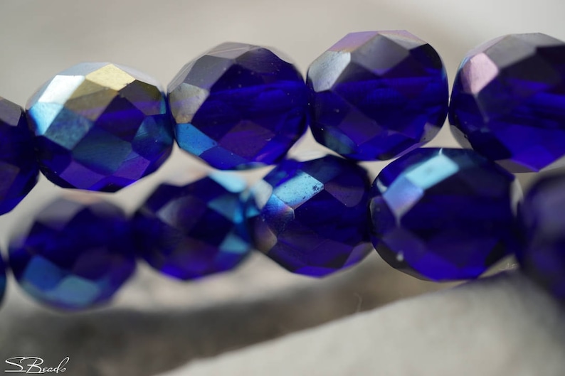 Puede incluir: Una hebra de cuentas de vidrio facetadas de color azul oscuro con brillo iridiscente. Las cuentas son redondas y tienen un dise&ntilde;o facetado.