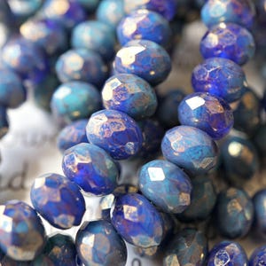 May include: Close-up of a strand of faceted beads in shades of blue and teal. The beads have a metallic sheen and a multi-faceted surface, creating a sparkling effect. These beads are ideal for jewelry making.