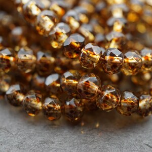 May include: A strand of amber glass beads with a faceted, teardrop shape. The beads have a translucent, golden brown colour.