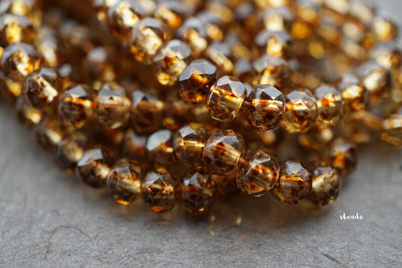 May include: A strand of amber glass beads with a faceted, teardrop shape. The beads have a translucent, golden brown colour.