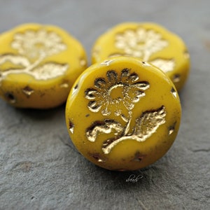 May include: Three yellow glass beads with gold floral designs. The beads are round and have a smooth, glossy finish.