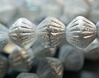 May include: Close-up of silver-colored beads with a textured, ribbed surface. The beads are arranged in a row, with the focus on the center bead.