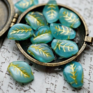 Peut inclure: Un ensemble de perles en verre bleu turquoise avec des accents de feuille d'or en forme de feuilles. Les perles sont dans un petit récipient rond en laiton avec un couvercle à charnière.