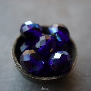 Puede incluir: Un peque&ntilde;o cuenco lleno de cuentas de vidrio facetadas de color azul iridiscente. Las cuentas son redondas y tienen un acabado brillante.