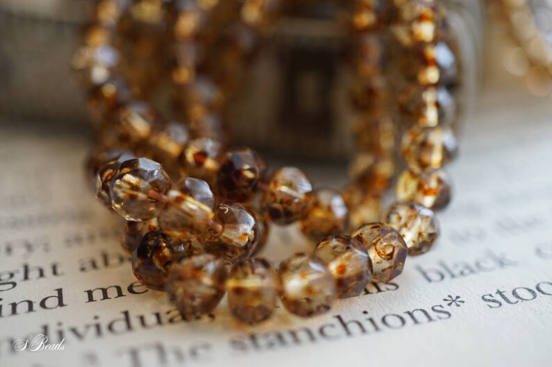 May include: A strand of brown faceted glass beads with a mottled, cloudy appearance. The beads are strung together on a clear thread and are arranged in a loose, flowing pattern.
