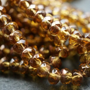 May include: A close-up of a strand of amber glass beads. The beads are faceted and have a shiny, translucent finish.
