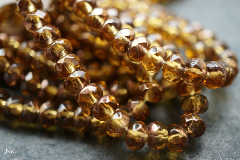 May include: A close-up of a strand of amber glass beads. The beads are faceted and have a shiny, translucent finish.