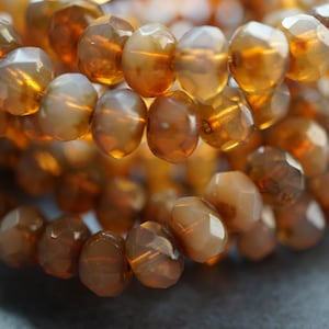 May include: A close-up of a strand of amber-colored faceted glass beads. The beads are arranged in a circular pattern, creating a shimmering effect.
