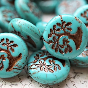 Op de afbeelding: Turquoise blauwe glazen kralen met een koperkleurig boomontwerp. De kralen zijn ovaalvormig en hebben een licht getextureerd oppervlak.
