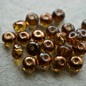 May include: A collection of small, faceted glass beads in shades of brown and gold. The beads have a metallic sheen and are arranged in a loose pile.