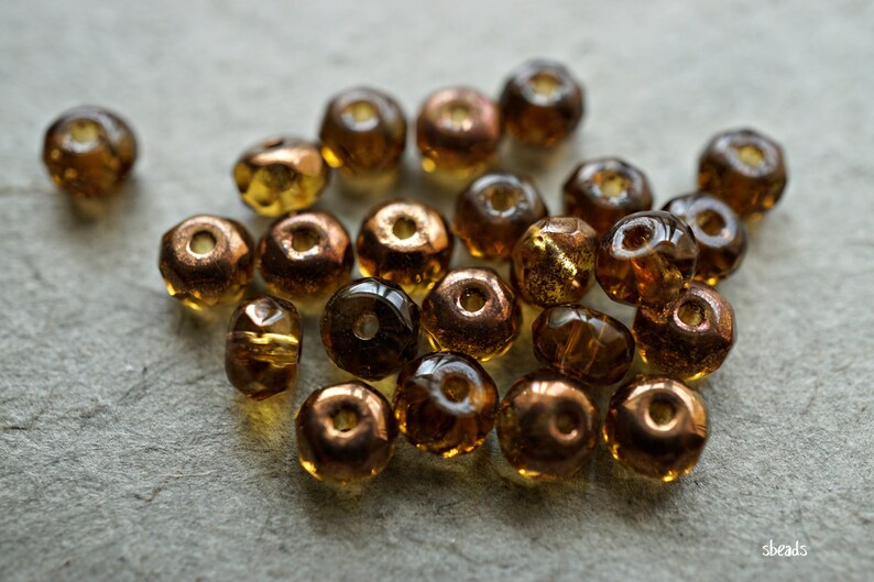 May include: A collection of small, faceted glass beads in shades of brown and gold. The beads have a metallic sheen and are arranged in a loose pile.