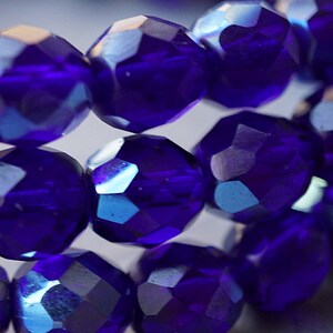 Puede incluir: Primer plano de una hebra de cuentas de vidrio facetadas de color azul iridiscente. Las cuentas son redondas y tienen una superficie brillante y reflectante.