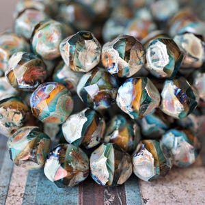 May include: A collection of faceted glass beads in shades of blue, brown, and white. The beads have an irregular, geometric shape and a glossy finish. The beads are clustered together, creating a textured and colorful display.