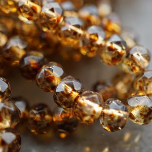 May include: A strand of faceted glass beads in a warm amber colour with brown flecks. The beads are round and have a shiny finish.