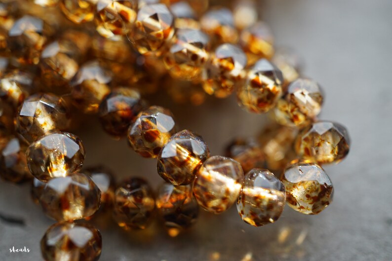 May include: A strand of faceted glass beads in a warm amber colour with brown flecks. The beads are round and have a shiny finish.