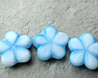 May include: Three blue and white flower-shaped glass beads. The beads have a white center and a blue outline.