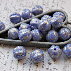 Peut inclure: Un plat en forme de cœur rempli de perles de verre bleues avec des reflets dorés. Les perles sont rondes et ont une surface texturée.