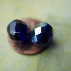 Puede incluir: Dos cuentas de vidrio facetadas de color azul oscuro, una ligeramente desenfocada, descansando sobre un centavo de cobre.