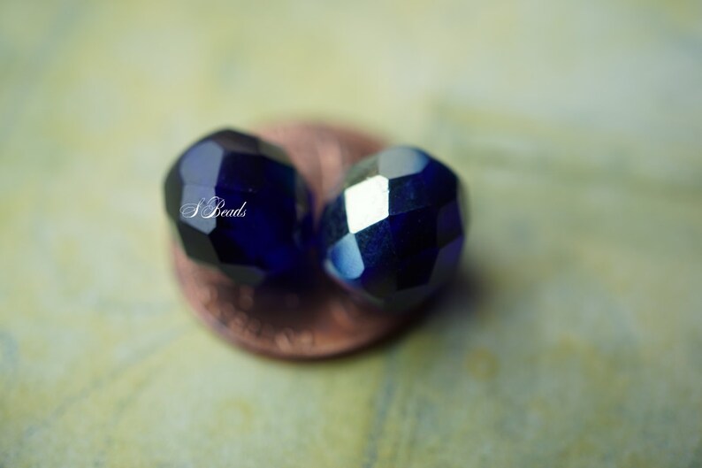 Puede incluir: Dos cuentas de vidrio facetadas de color azul oscuro, una ligeramente desenfocada, descansando sobre un centavo de cobre.
