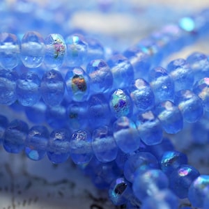 Könnte beinhalten: Eine Strähne aus irisierenden blauen Glasperlen. Die Perlen sind facettiert und haben eine matte Oberfläche.