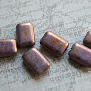 May include: Six iridescent purple and gold rectangular glass beads. The beads have a speckled, textured surface.