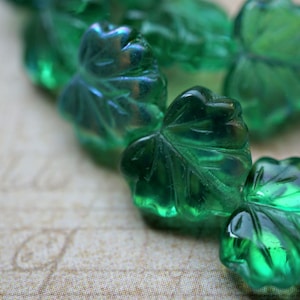 Può includere: Una collana di perline di vetro verde a forma di foglie. Le perline hanno una finitura leggermente iridescente.
