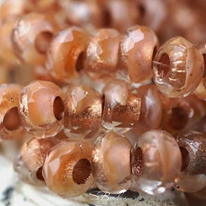 May include: Close-up of a strand of translucent peach-colored glass beads with copper flecks. The beads are faceted and have a hole running through the center.