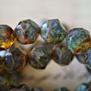 May include: Close-up of a strand of faceted beads. The beads have a mix of colors, including green, brown, and hints of blue and gold. The beads have a unique, irregular shape and a glossy finish.