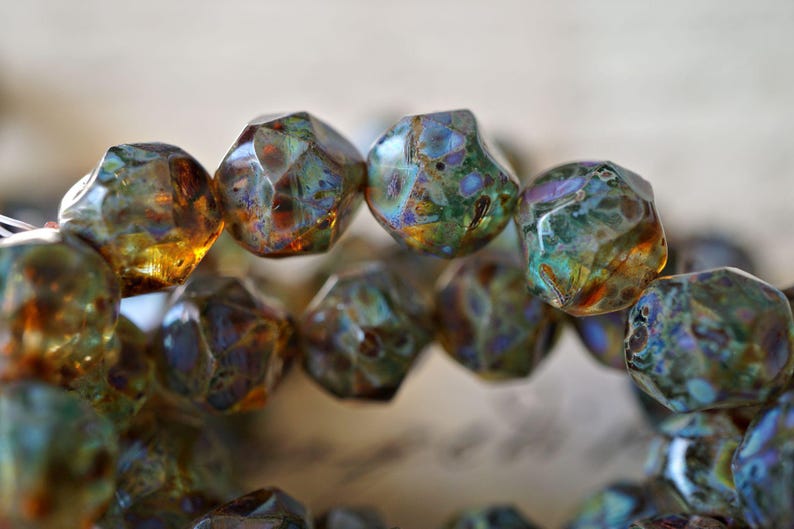 May include: Close-up of a strand of faceted beads. The beads have a mix of colors, including green, brown, and hints of blue and gold. The beads have a unique, irregular shape and a glossy finish.