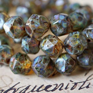 May include: Close-up of a collection of faceted beads. The beads have a mix of colors, including brown, blue, and gold. The beads are irregularly shaped and have a textured surface. The beads are likely used for jewelry making.