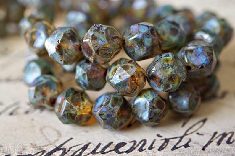 May include: Close-up of a collection of faceted beads. The beads have a mix of colors, including brown, blue, and gold. The beads are irregularly shaped and have a textured surface. The beads are likely used for jewelry making.