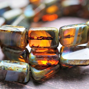 May include: A close-up of a strand of colorful glass beads. The beads are rectangular and have a mottled, iridescent finish. The colors are a mix of brown, green, blue, and orange.