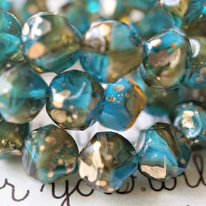 May include: Close-up of a strand of faceted beads. The beads are a mix of teal, blue, and gold. The beads have an irregular shape and are strung together. The background has the words "for you" in cursive.