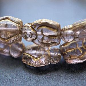 May include: A close-up of a gold-toned necklace with a repeating pattern of small, detailed figures. The figures are carved into the beads and have a textured surface.